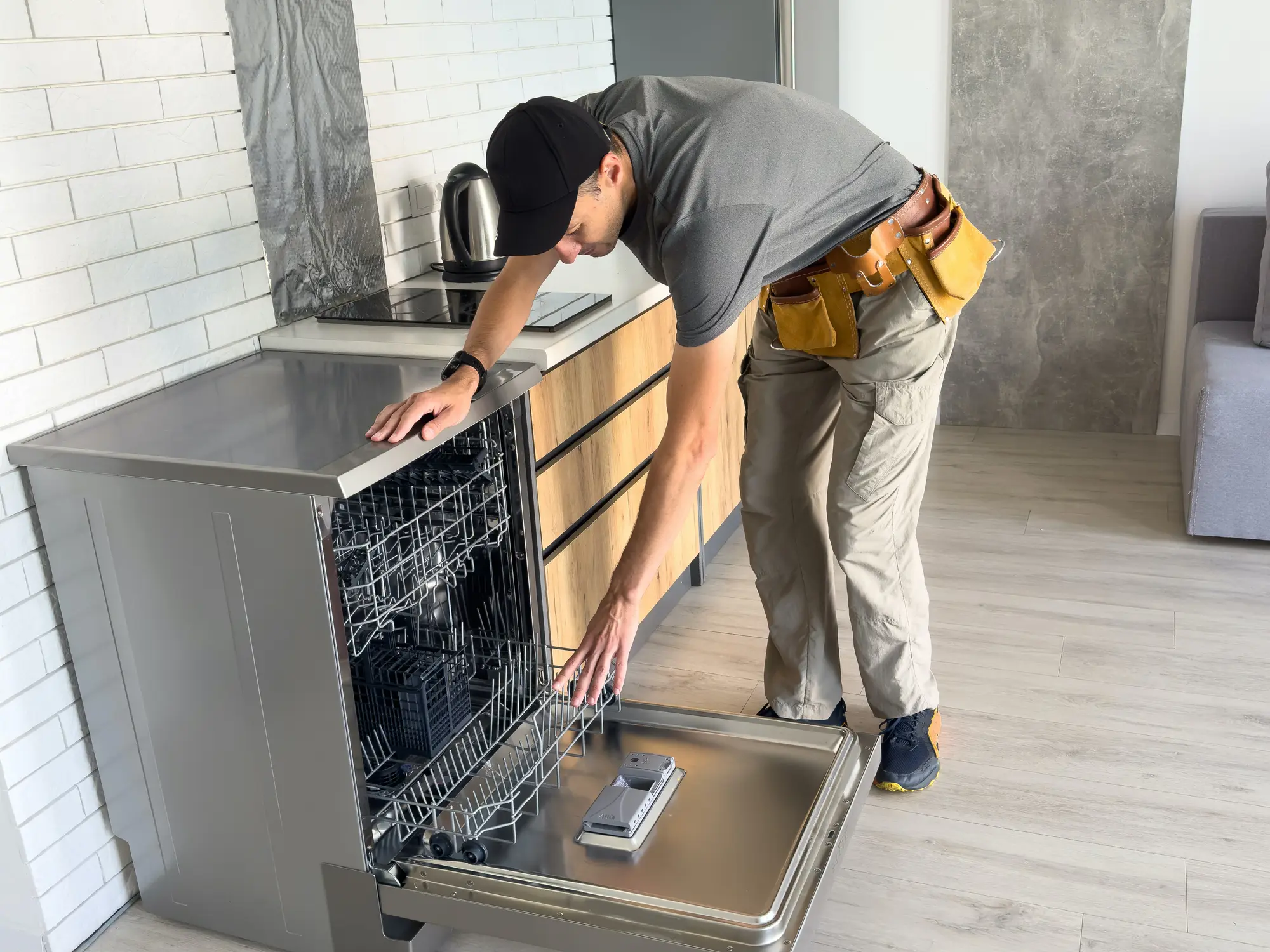 Young Repairman Service Worker Repairing Dishwasher Appliance In Kitchen Technician inspecting dishwasher in modern kitchen.
